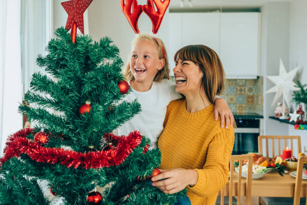 Cute little girl decorating the Christmas tree with her beautiful mother.