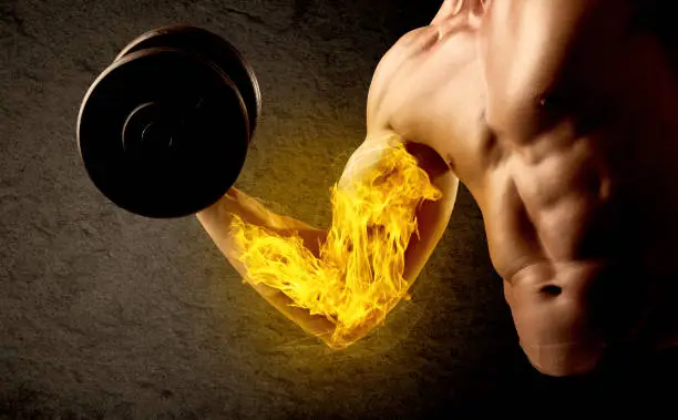 Photo of Muscular bodybuilder lifting weight with flaming biceps concept