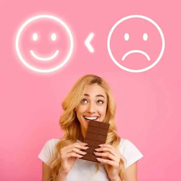 Happy Pretty Woman Eating Chocolate To Be In A Good Mood. Pink background.