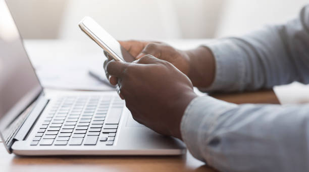 istock Unrecognizable man browsing smartphone and working on laptop at desk 1187578091