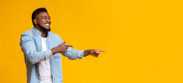Joyful black guy pointing two fingers aside at copy space