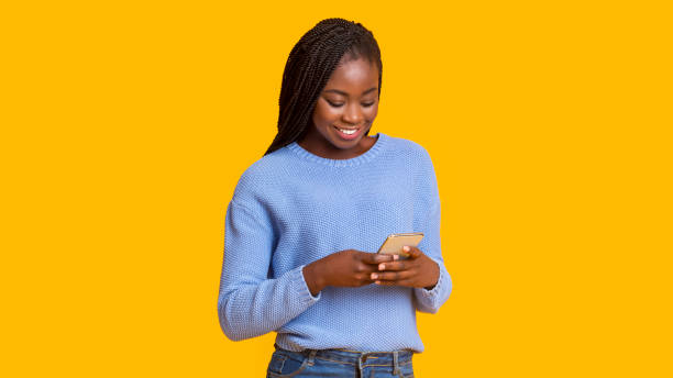 istock Smiling african-american woman using smartphone on yellow background 1187578813