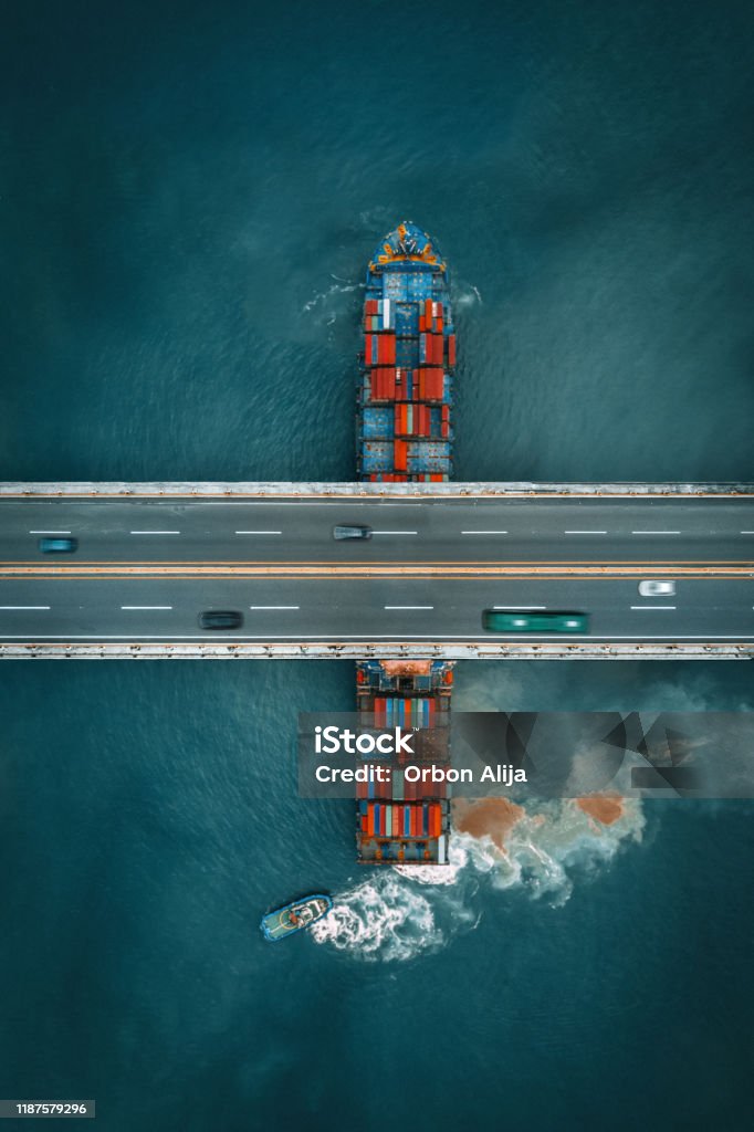 Container freight ship sailing under a road bridge Freight Transportation Stock Photo