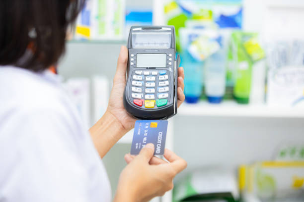 payer avec une carte de crédit, faire des achats de nombreux médicaments, payer avec un crédit sur de nombreux médicaments étagère dans le fond de la pharmacie. - pharmacy credit card pharmacist people photos et images de collection