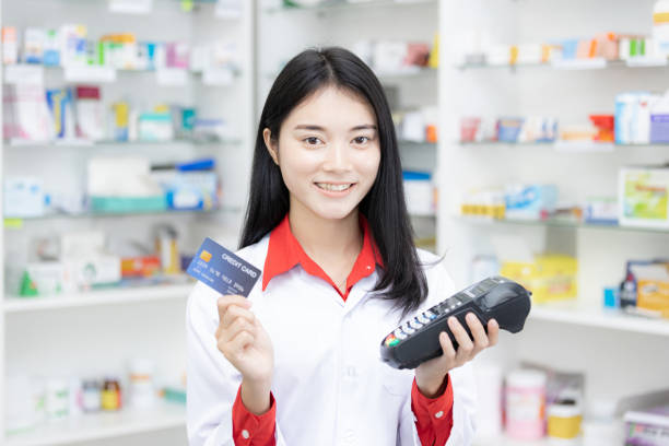 payer avec une carte de crédit, faire des achats de nombreux médicaments, payer avec un crédit sur de nombreux médicaments étagère dans le fond de la pharmacie. - pharmacy credit card pharmacist people photos et images de collection