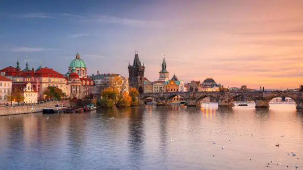 Panoramic cityscape image of famous Charles Bridge in Prague during beautiful autumn sunset.