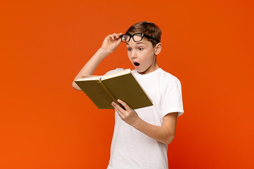 Shocked teen boy surprised by the twists and turn of story, orange background