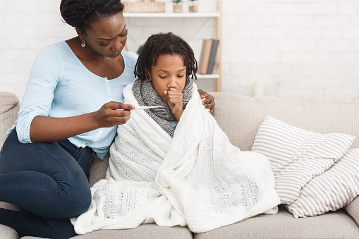 Caring African Mom Checking Temperature Of Her Sick Child At Home, Girl In Blanket