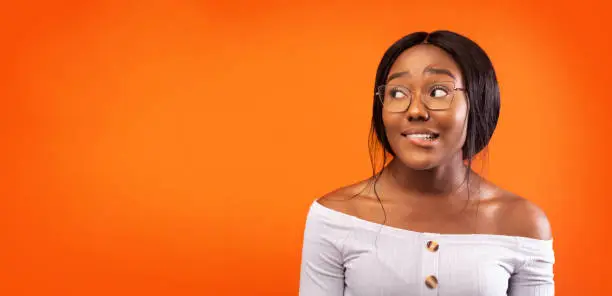 Photo of Afro Girl Biting Lips Standing Over Orange Studio Background, Panorama