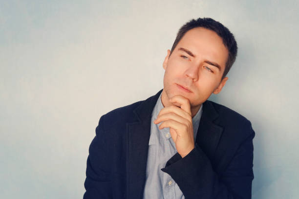 istock A young businessman in a thoughtful pose reflects on business. Thinking through ideas and plans. A grown guy on a blue background. Thoughtful handsome male 1187582559