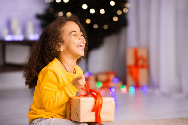 aufgeregt afrikanische mädchen lachen mit weihnachtsgeschenk - kinderwunsch stock-fotos und bilder