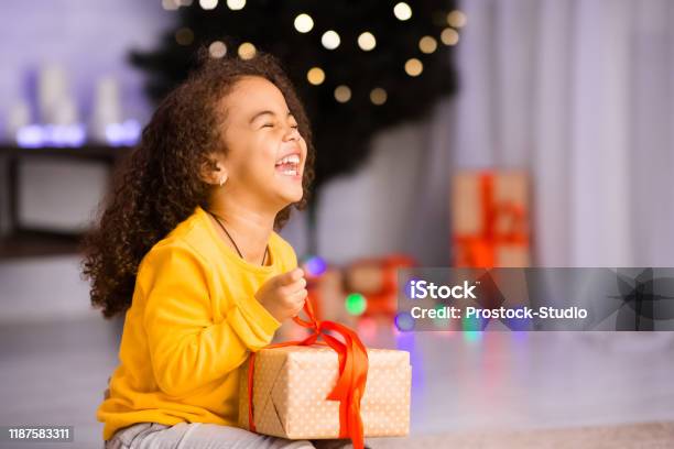 Excited African Girl Laughing With Christmas Gift Stock Photo - Download Image Now - Child, Christmas, Gift
