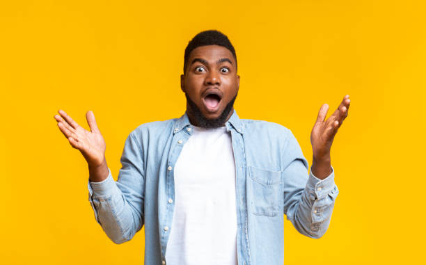Surprised black man standing with opened mouth and raised hands