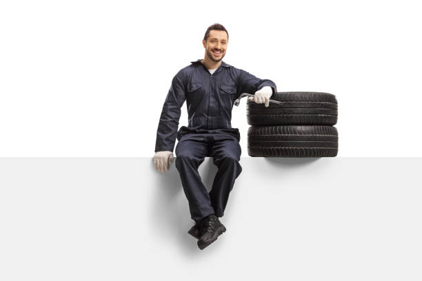 istock Auto mechanic sitting on a panel with tires and a wrench 1187583400