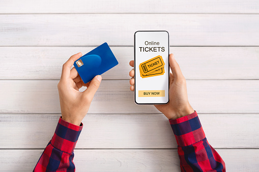 Man buying event tickets with app on smartphone and credit card, white wooden background with free space