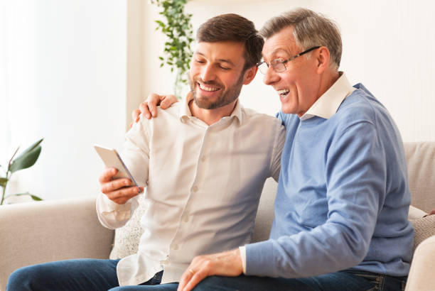 istock Son Teaching Senior Father Use Phone Sitting On Sofa Indoor 1187584788