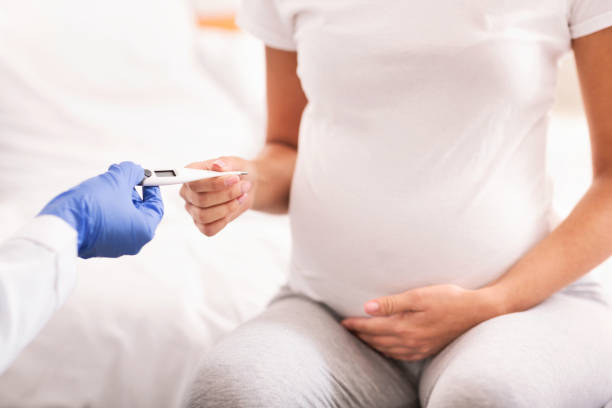 femme enceinte méconnaissable prenant le thermomètre de la main du docteur s'asseyant à l'intérieur - thermometer cold fever focus photos et images de collection