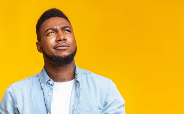 Portrait of suspicious black guy looking upwards at copy space Portrait of suspicious black guy looking upwards at copy space on yellow background. sneering stock pictures, royalty-free photos & images