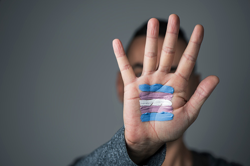 closeup of the palm of the hand of a young caucasian person with a transgender flag painted in it, in front of his or her face