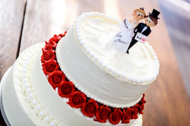 White wedding cake with bride and groom figurines on top. White wedding cake with bride and groom figurines on top. Beautiful white wedding cake with red roses in the table with small husband and wife puppets on top. white wedding cake red roses stock pictures, royalty-free photos & images
