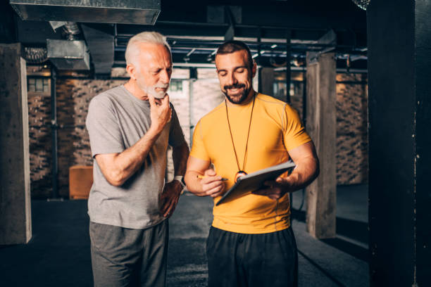 istock Personal coach showing a note with an exercise plan to an active elderly man in a training area of a gym 1187597696