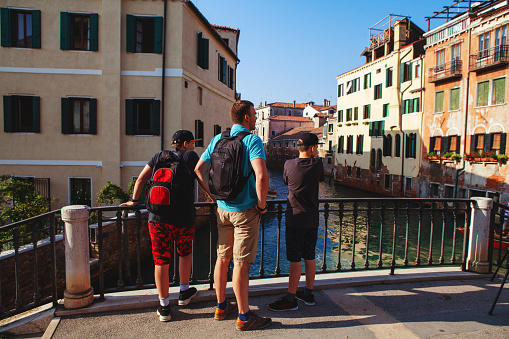 Venice, Italy - 27 October, 2019: father and two teenager kids stand on a canal bridge in Venice and look to one side