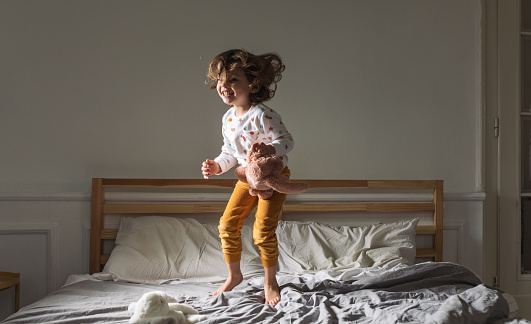 Adorable happy little girl in pajamas jumping on king-size bed in the morning.