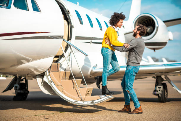 młoda bogata kobieta wkłada ręce na ramiona swojego partnera, gdy przygotowuje się do wyjścia z prywatnego samolotu zaparkowanego na płycie lotniska - high society audio zdjęcia i obrazy z banku zdjęć