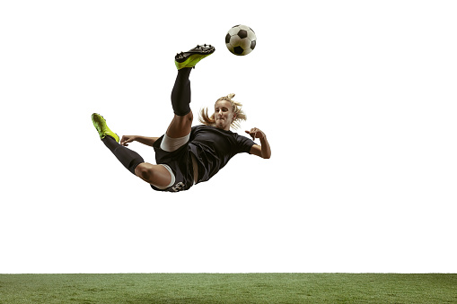Young female soccer or football player with long hair in sportwear and boots kicking ball for the goal in jump on white background. Concept of healthy lifestyle, professional sport, motion, movement.