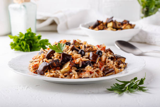 Eggplant pilaf served in white plate. Rice with aubergine,  black raisins and tomatoes on white table. Healthy vegetarian food concept. Eggplant pilaf served in white plate. Rice with aubergine,  black raisins and tomatoes on white table. Healthy vegetarian food concept. pilau rice stock pictures, royalty-free photos & images