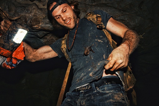 Young biologist covered in mud inside a cave carrying a small bat on his shirt