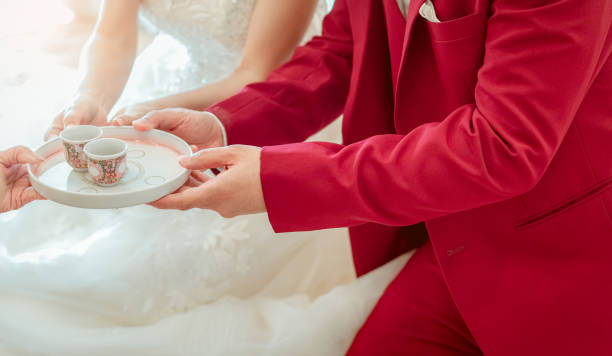 Groom and bride in tea ceremony on wedding ceremony day. Bride and groom in white wedding dress and red suit sit anf lifting tea cup. Marriage or matrimony. Begin couple life. Chinese wedding culture. novio y novia en la ceremonia del té en el día de la ceremonia de la boda. novia y novio en vestido de novia blanco y traje rojo sentarse anf lifting taza de té. matrimonio o matrimonio. empieza la vida en pareja. cultura de la boda china.