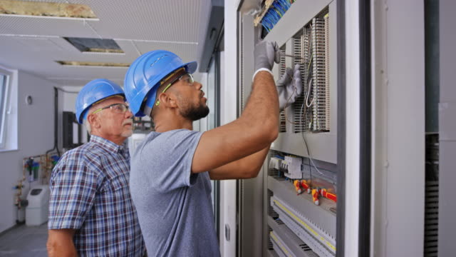 Male apprentice connecting the wires in the electrical panel under supervision of senior electrician