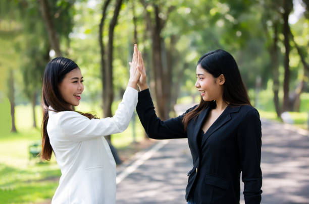 istock Smiling Young Women High-Fiving While Standing Against Trees 1187612340