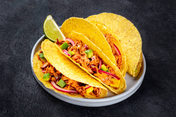 istock Cochinita pibil taco shells, a Mexican snack with pulled pork and avocado and marinated red onion, a close-up shot on a dark background 1187615164