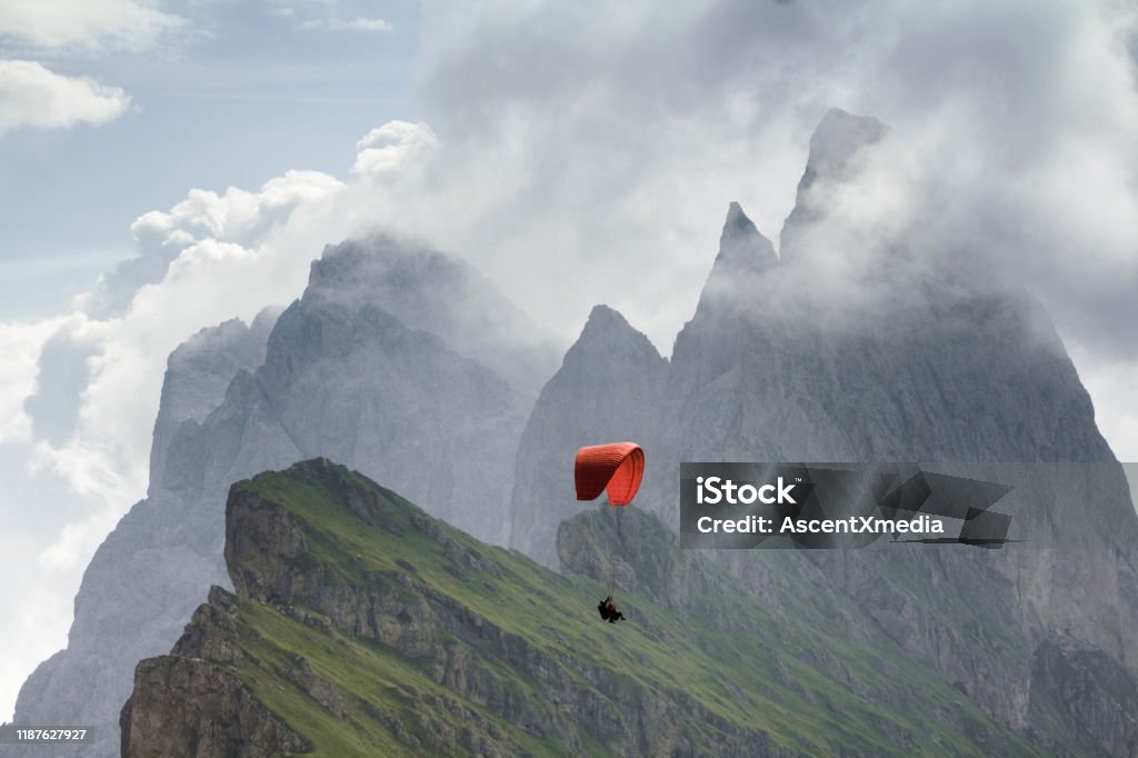Scenic view of paraglider flying through mountain valley Mountain peak and lofty clouds behind Paragliding Stock Photo