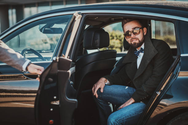 istock Busy nice businessman in sunglasses is talking by smartphone while his elegant assistant is opening door for him. 1187631697