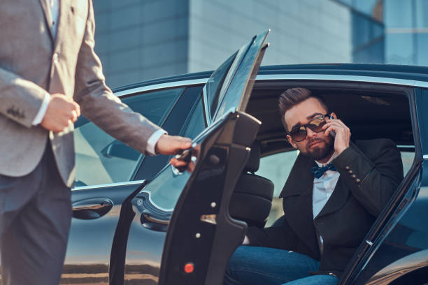 istock Busy businessman in sunglasses is talking by smartphone while his elegant assistant is opening door for him. 1187631784