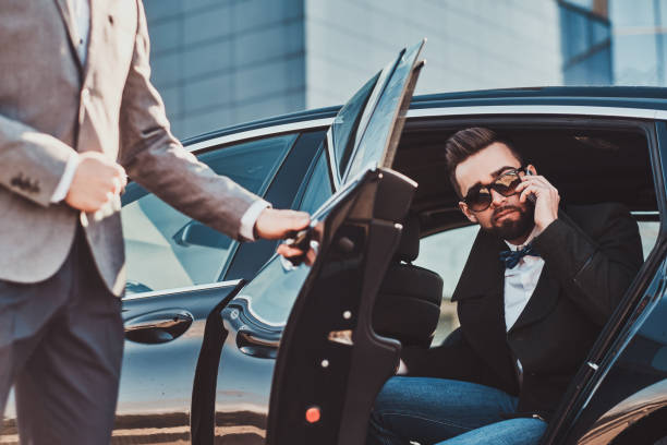istock Busy businessman in sunglasses is talking by smartphone while his elegant assistant is opening door for him. 1187631816