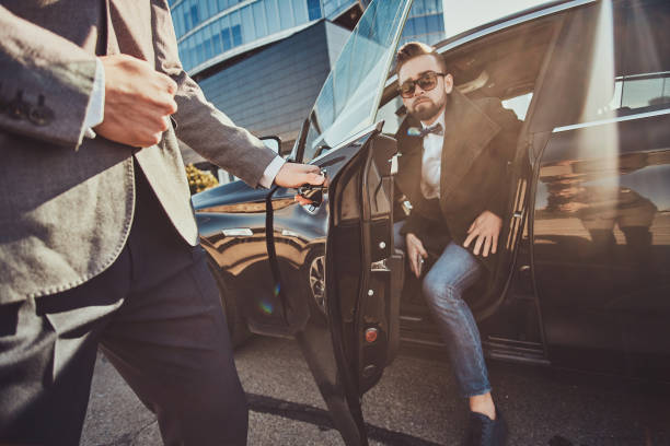 istock Busy businessman in sunglasses is talking by smartphone while his elegant assistant is opening door for him. 1187631832