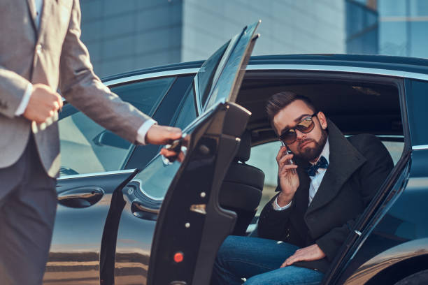 istock Busy businessman in sunglasses is talking by smartphone while his elegant assistant is opening door for him. 1187631934