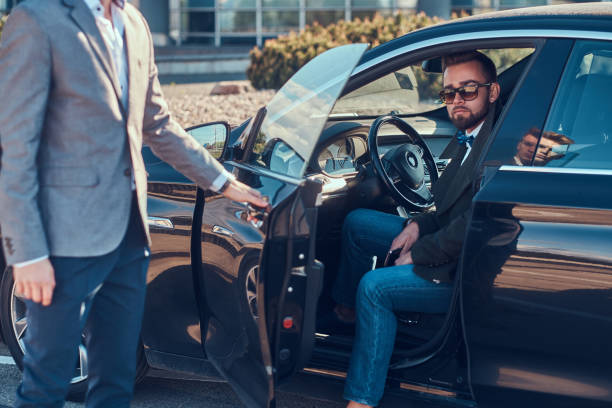 istock Businessman in sunglasses is talking by mobile phone while his young smart assistant is opening door for him. 1187632557