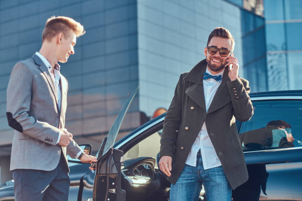 istock Businessman in sunglasses is talking by mobile phone while his young smart assistant is opening door for him. 1187632603