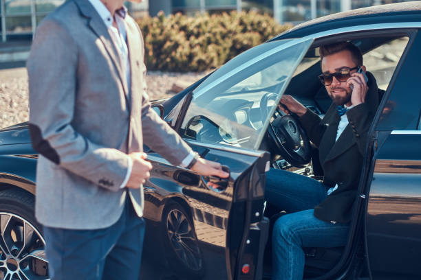 istock Businessman in sunglasses is talking by mobile phone while his young smart assistant is opening door for him. 1187632741