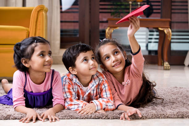 Children playing with paper airplane at home Happy children playing with toy paper airplane on carpet at home childrens day photos stock pictures, royalty-free photos & images