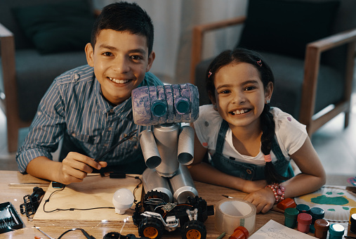 Portrait of two adorable young siblings posing with their newly built toy robot at home