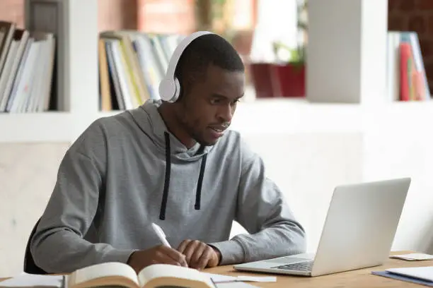 Photo of African guy e-learning seated at desk in public library