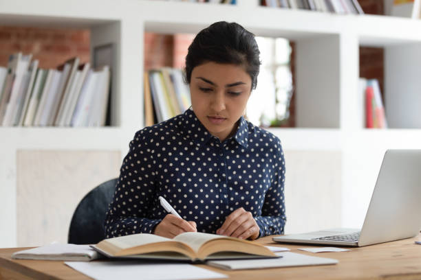 istock Indian ethnicity student woman writing notes reading textbook studying indoors 1187643128