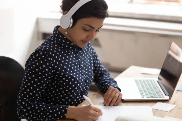 Photo of Indian ethnicity woman wearing headphones listens educational course studying online