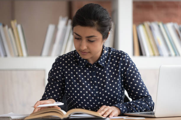 istock Indian student sitting at desk turn the pages search information 1187643146